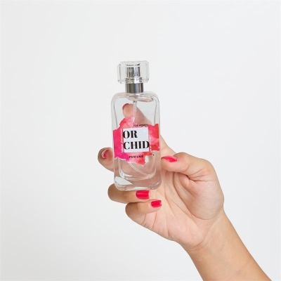 Frasco transparente de perfume OR CHID com tampa acrílica, mão feminina com unhas vermelhas a segurá-lo