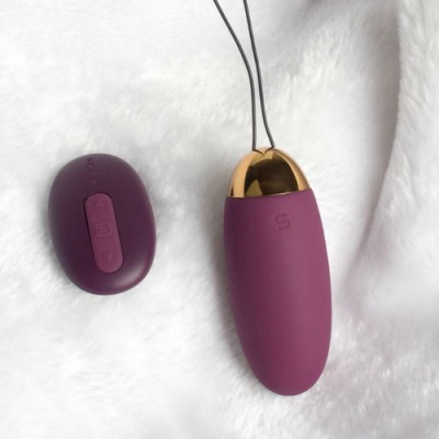 Dispositivo oval roxo com parte dourada e controlo remoto sobre tecido branco