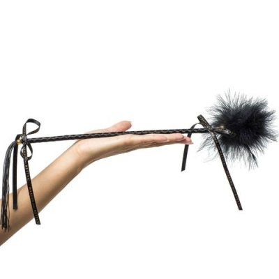 Chicote preto com pompa felpuda e fitas segurado por mão humana