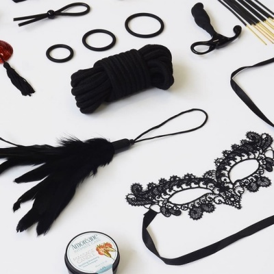 Acessórios BDSM em preto dispostos sobre fundo branco.