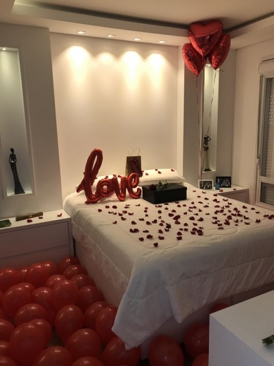 Quarto decorado com balões vermelhos e confetes de amor sobre cama branca