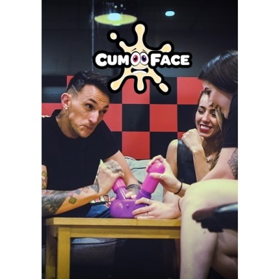 Jogo de braço de ferro com mãos de silicone cor-de-rosa num suporte roxo com texto 'CUM FACE' e pessoas à volta de mesa