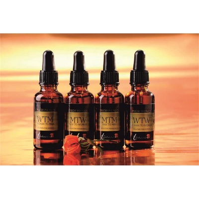 Quatro frascos âmbar com conta-gotas e etiquetas douradas sobre superfície castanha com flores.