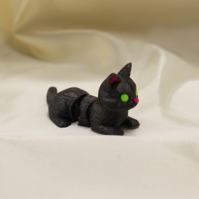 Figura de gato preto articulado com olhos verdes e nariz rosa em tecido branco