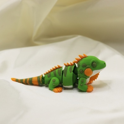 Brinquedo articulado de dinossauro verde e laranja sobre tecido branco