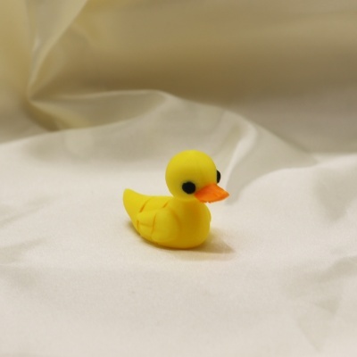 Brinquedo pato amarelo com bico laranja sobre tecido branco