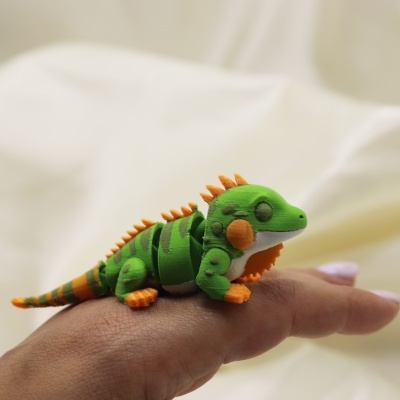 Miniatura de lagarto verde e laranja sobre dedo humano