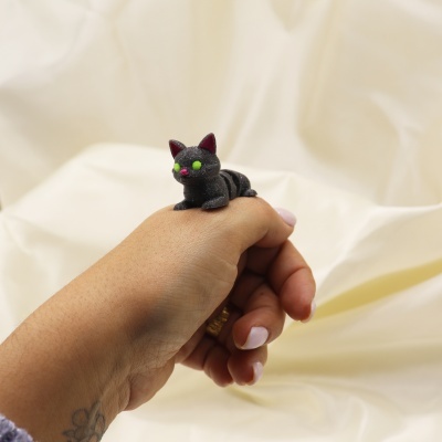Anel gatinho preto fluorescente numa mão com unhas pintadas de rosa claro