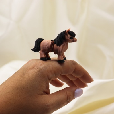 Anel com cavalo castanho e preto no dedo médio de mão com unha lilás.