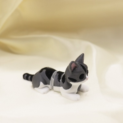 Figura de gato em plástico preto, cinzento e branco sobre tecido branco
