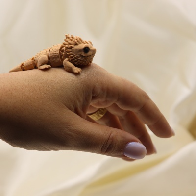 Figura articulada de dragão bege sobre mão com anel e unhas lilás