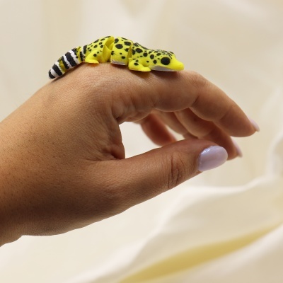 Anel de lagarto amarelo e preto em dedo com unhas roxas claras