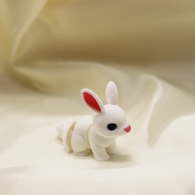 Figurinha de coelho branco com orelhas vermelhas sobre tecido creme.