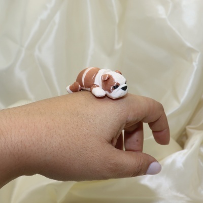 Miniatura de bulldog castanho e branco repousando numa mão com unhas brancas, fundo creme amarfanhado.