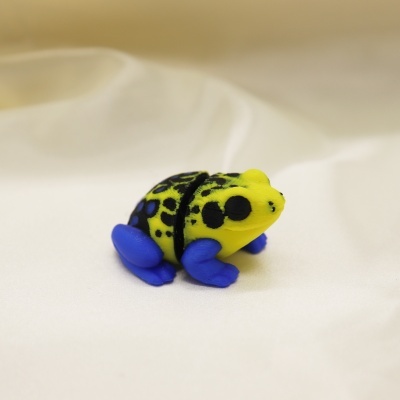 Brinquedo de sapo amarelo com manchas pretas e pernas azuis sobre tecido branco