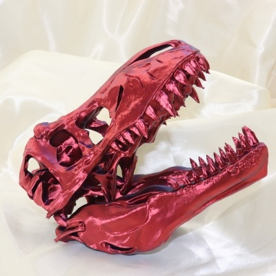 Crânio decorativo vermelho metálico de dinossauro sobre tecido branco