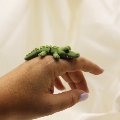 Anel em forma de crocodilo verde num dedo da mão.
