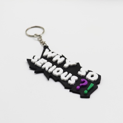 Chaveiro preto com texto branco WHY SO SERIOUS? e símbolos roxo e verde