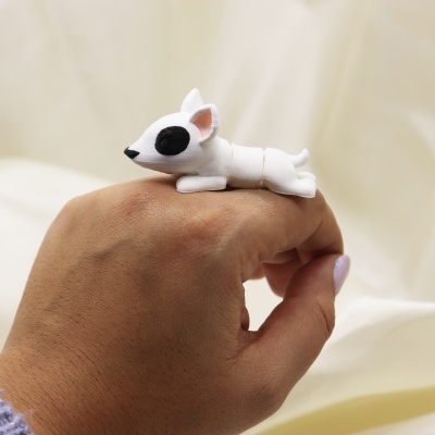 Anel em forma de cão branco com manchas negras no dedo de uma mão.