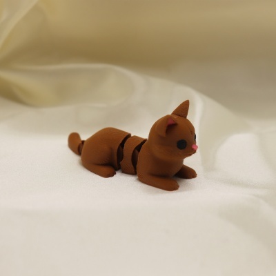 Figura de gato castanho de plástico articulado sobre tecido branco.