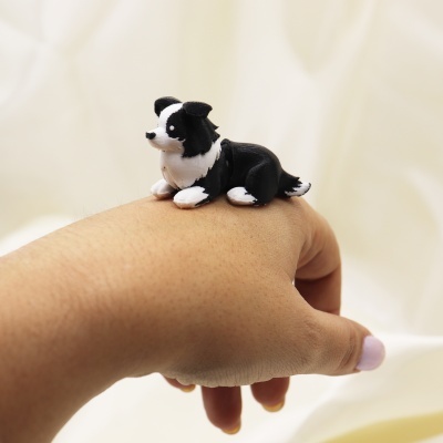 Anel em forma de cão preto e branco num dedo de mão com unhas pintadas