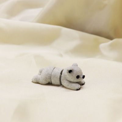 Figura pequena de panda cinzenta com manchas negras sobre tecido creme