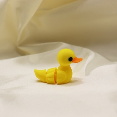 Pato amarelo de plástico com bico laranja e olhos pretos sobre tecido branco