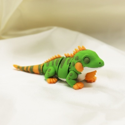 Figura de lagarto verde e laranja em plástico sobre tecido branco