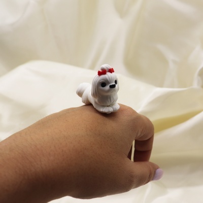Anel com figura de cão branco e laços vermelhos numa mão.