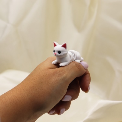 Anel com gato branco de plástico numa mão com unhas cor-de-rosa.