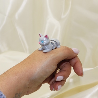 Anel com figura de gato cinzento em mão feminina sobre fundo de tecido creme