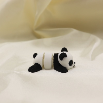Figura decorativa em forma de panda deitado preto e branco sobre tecido branco.