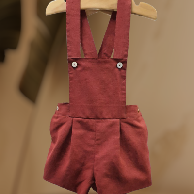 Macacão de criança cor de ferrugem com botões brancos e suspensórios cruzados