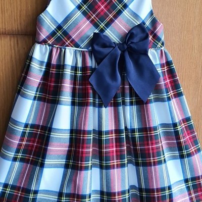 Vestido infantil xadrez com laço azul escuro pendurado num cabide