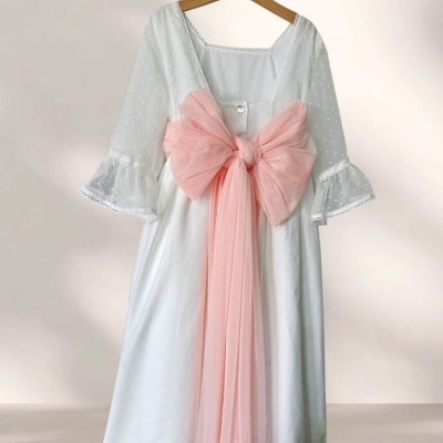 Vestido branco com laço rosa pendurado num cabide de madeira