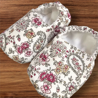 Pantufas florais em tecido creme com padrão de flores coloridas.