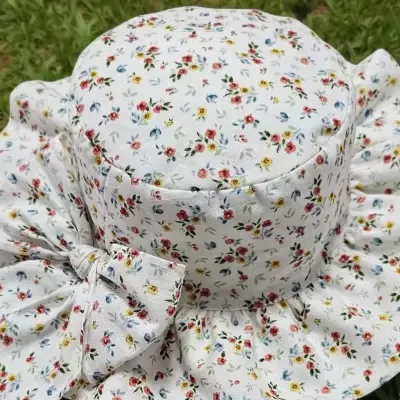 Chapéu branco com flores coloridas e laço, sobre relva com margaridas