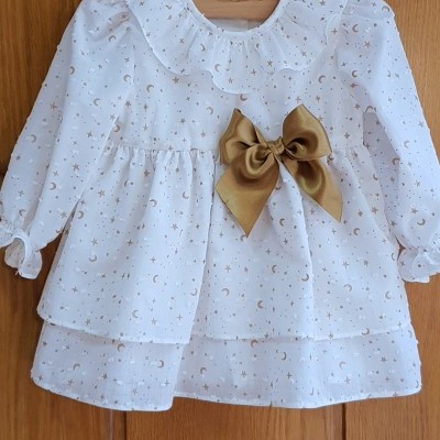 Vestido branco com padrão de estrelas e luas douradas e laço castanho dourado