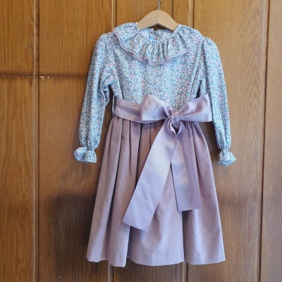 Vestido infantil floral com saia rosa velha e laço grande pendurado em cabide de madeira