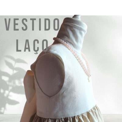 Vestido infantil branco e bege com laço grande nas costas num manequim