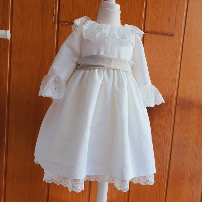 Vestido branco de bebê com renda e faixa cinza num manequim