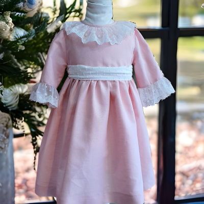 Vestido infantil rosa com renda branca e cinto, em manequim junto a janela com decoração natalícia