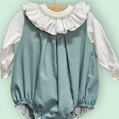 Babygrow azul com gola branca em folho bordada, manga comprida e punhos elásticos pendurado em cabide de madeira