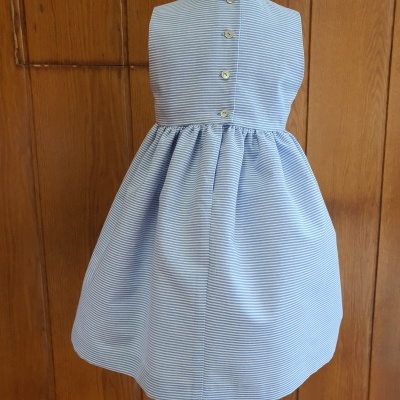 Vestido azul com riscas brancas e botões, pendurado numa porta de madeira