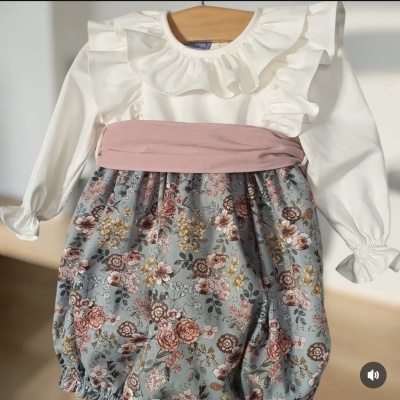 Roupa de bebé branca com folhos e parte inferior floral suspensa numa cabide