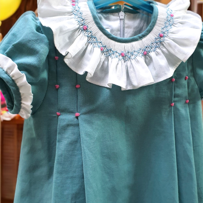 Vestido infantil azul esverdeado com babados brancos na gola e bordados coloridos