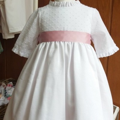 Vestido branco de criança com fita rosa, mangas 3/4 com babados, em manequim