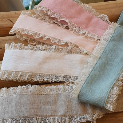 Cinco fitas de tecido em cores pastel com bordas de renda branca sobre madeira