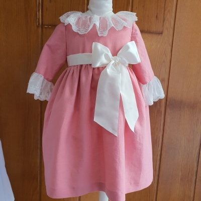 Vestido infantil cor-de-rosa com gola e punhos em renda branca e laço branco largo na cintura