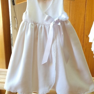 Vestido branco de criança com laço e textura especial pendurado em cabide